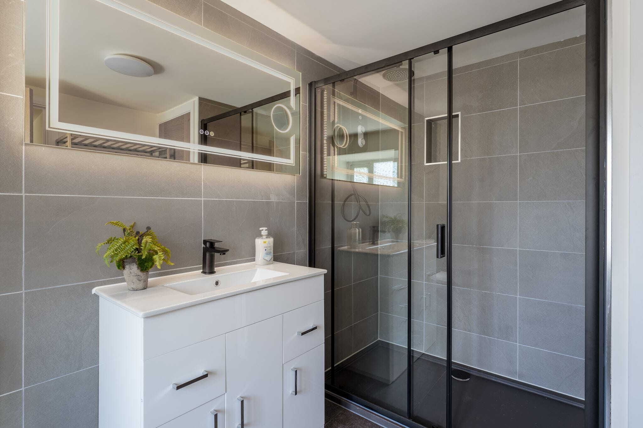 Une salle de bain moderne avec un meuble-lavabo blanc, un grand miroir et une douche à parois de verre.
