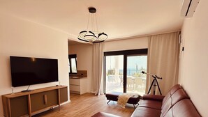 A modern living room with a flat-screen TV, leather sofa, and a balcony with a view. - Serenity House—Private Infinity Pool, Panoramic Sea Views, and Near Budva (Krimovica)