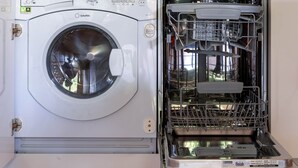Una cucina compatta con lavatrice e asciugatrice integrate, una macchina del caffè e un piccolo vaso con fiori sul piano di lavoro.