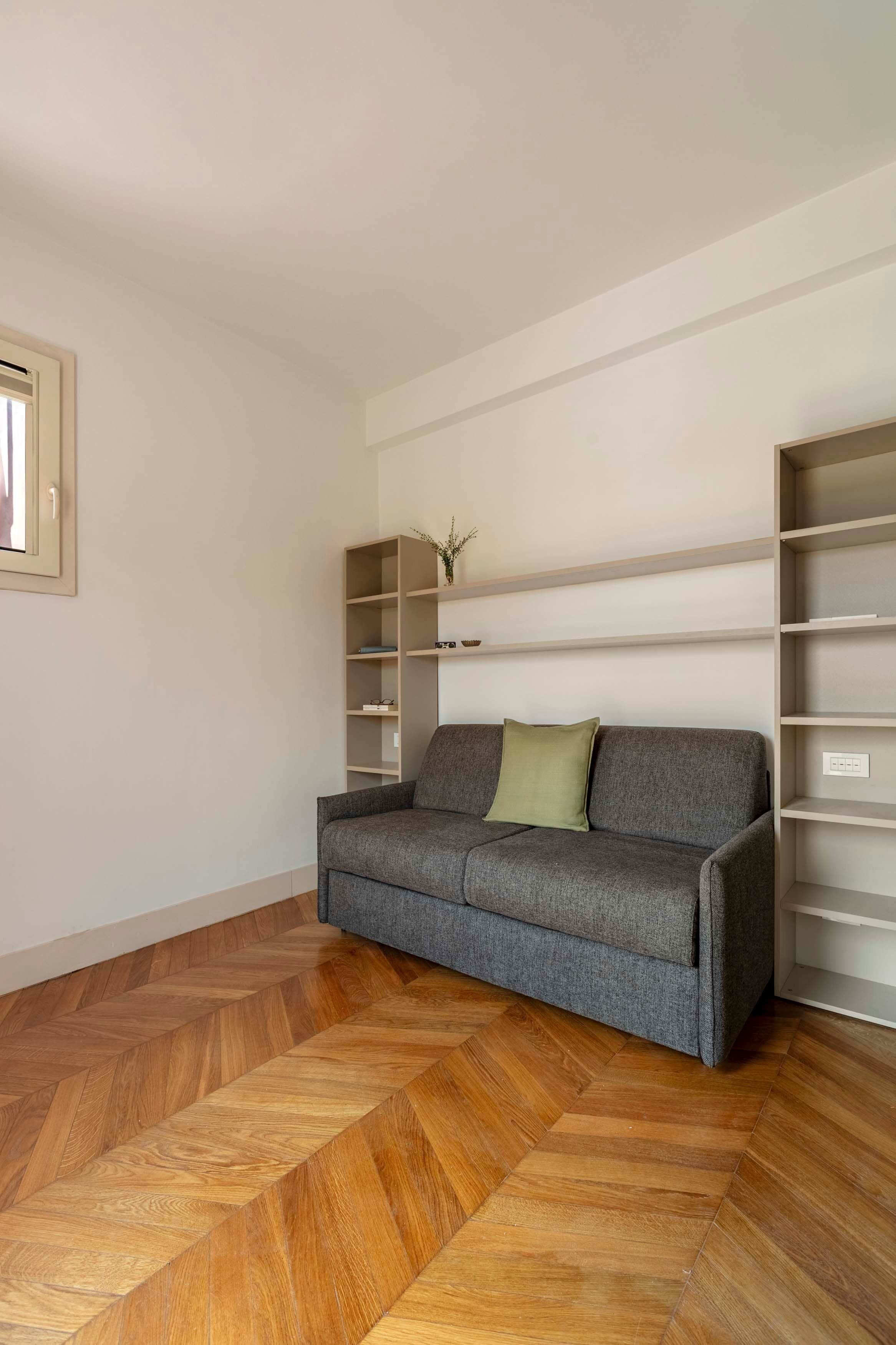 Una habitació amb un sofà gris, terres de parquet i mobles de paret.