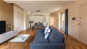 A modern living room with a sofa, a coffee table, and a TV. There is a dining area with chairs and a table in the background. - Comfort & Luxury at the Colosseum - Entire Apartment (Rome)