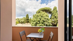 A balcony with a table and chairs, a vase of flowers, and a view of trees and a clear sky. - Comfort & Luxury at the Colosseum - Entire Apartment (Rome)
