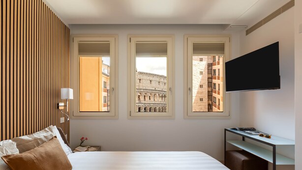 A hotel room with a bed, a desk, and three windows offering views of historical architecture. - Comfort & Luxury at the Colosseum - Entire Apartment (Rome)