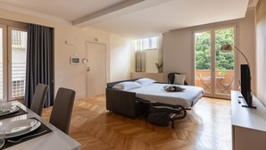 A modern hotel room with a bed, a desk, a chair, a dining table, and a balcony with a table and chairs. - Comfort & Luxury at the Colosseum - Entire Apartment (Rome)