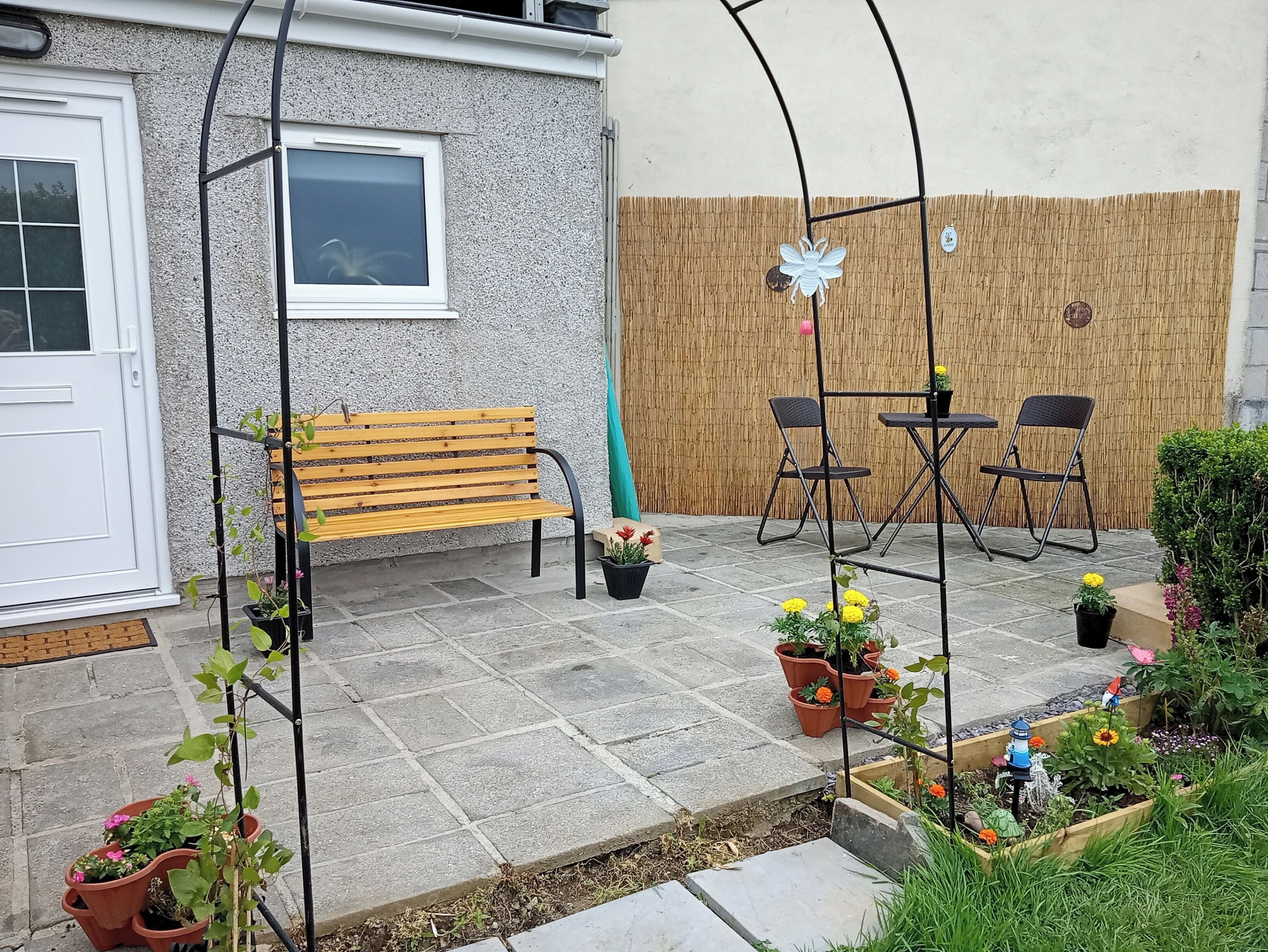 Un patio con un banco de madera, dos sillas, una mesa y plantas en macetas.
