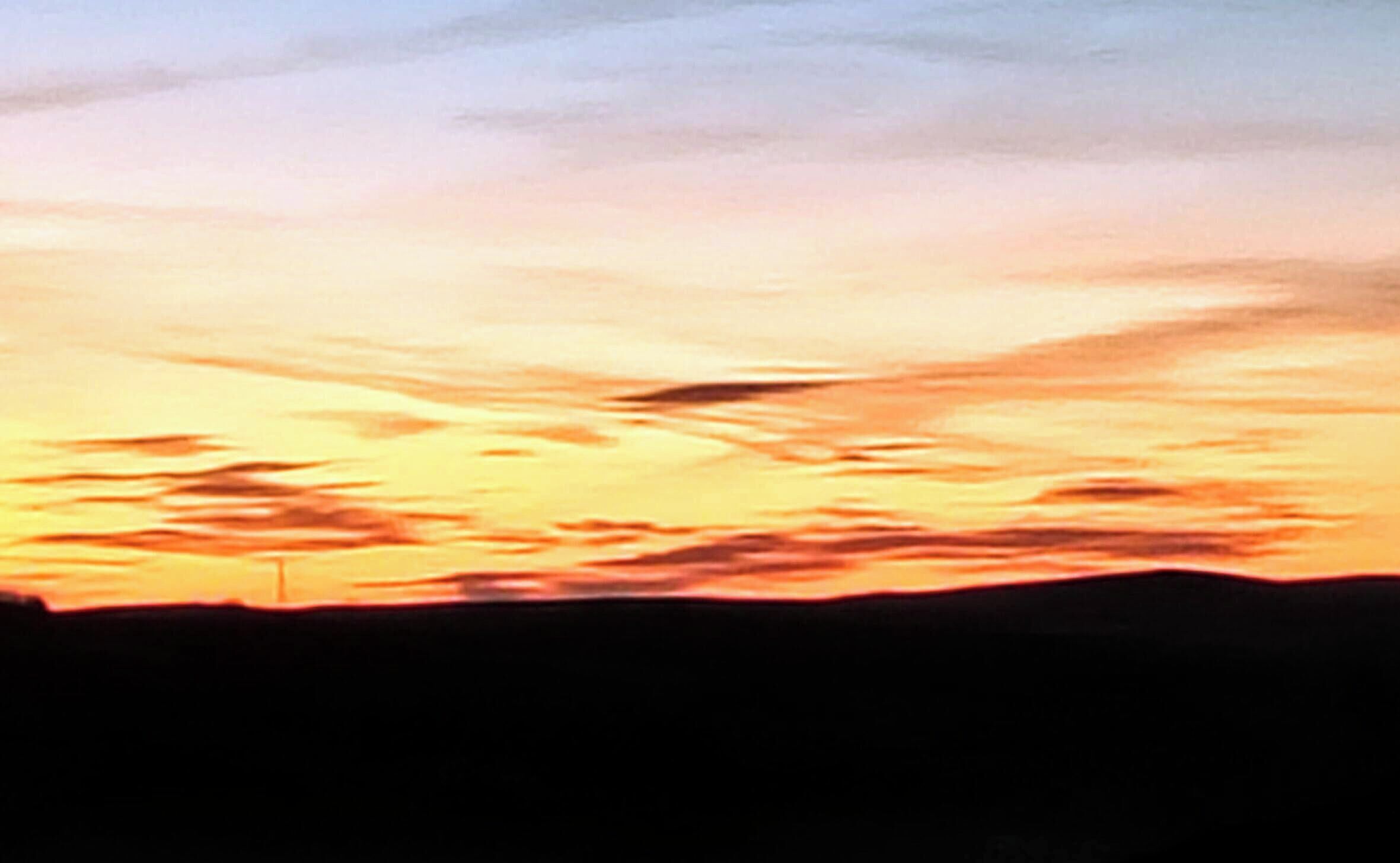 Un coucher de soleil avec la silhouette d’un paysage.
