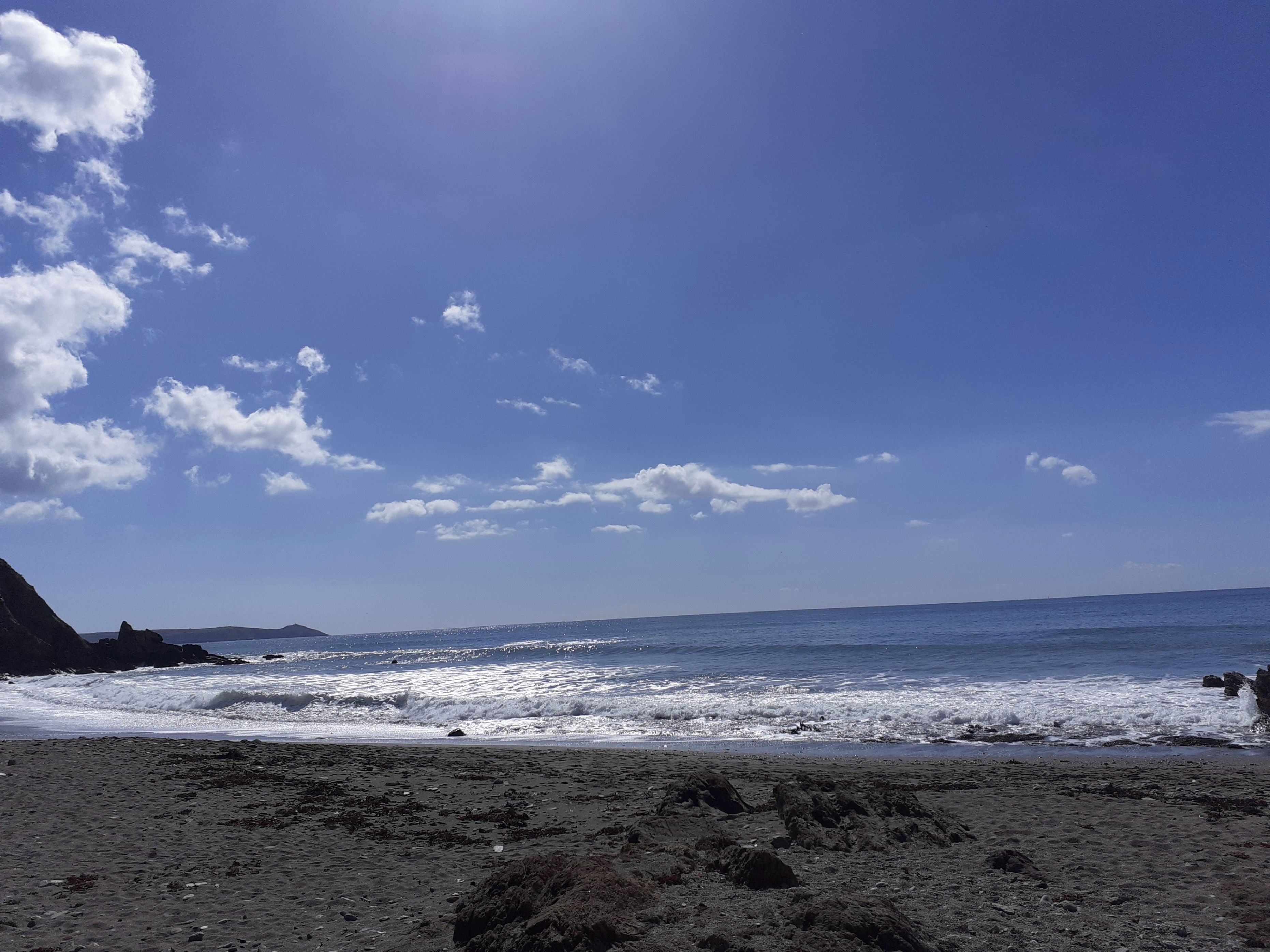Una platja amb onades, cel blau i una muntanya allunyada.