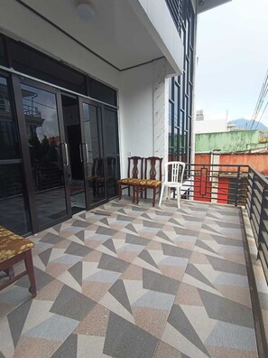 A balcony with patterned flooring, a wooden bench, and a white chair.