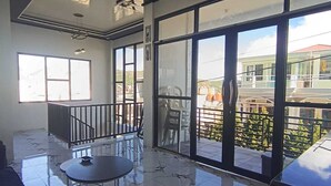 A spacious indoor area with large windows, a balcony, and a tiled floor.