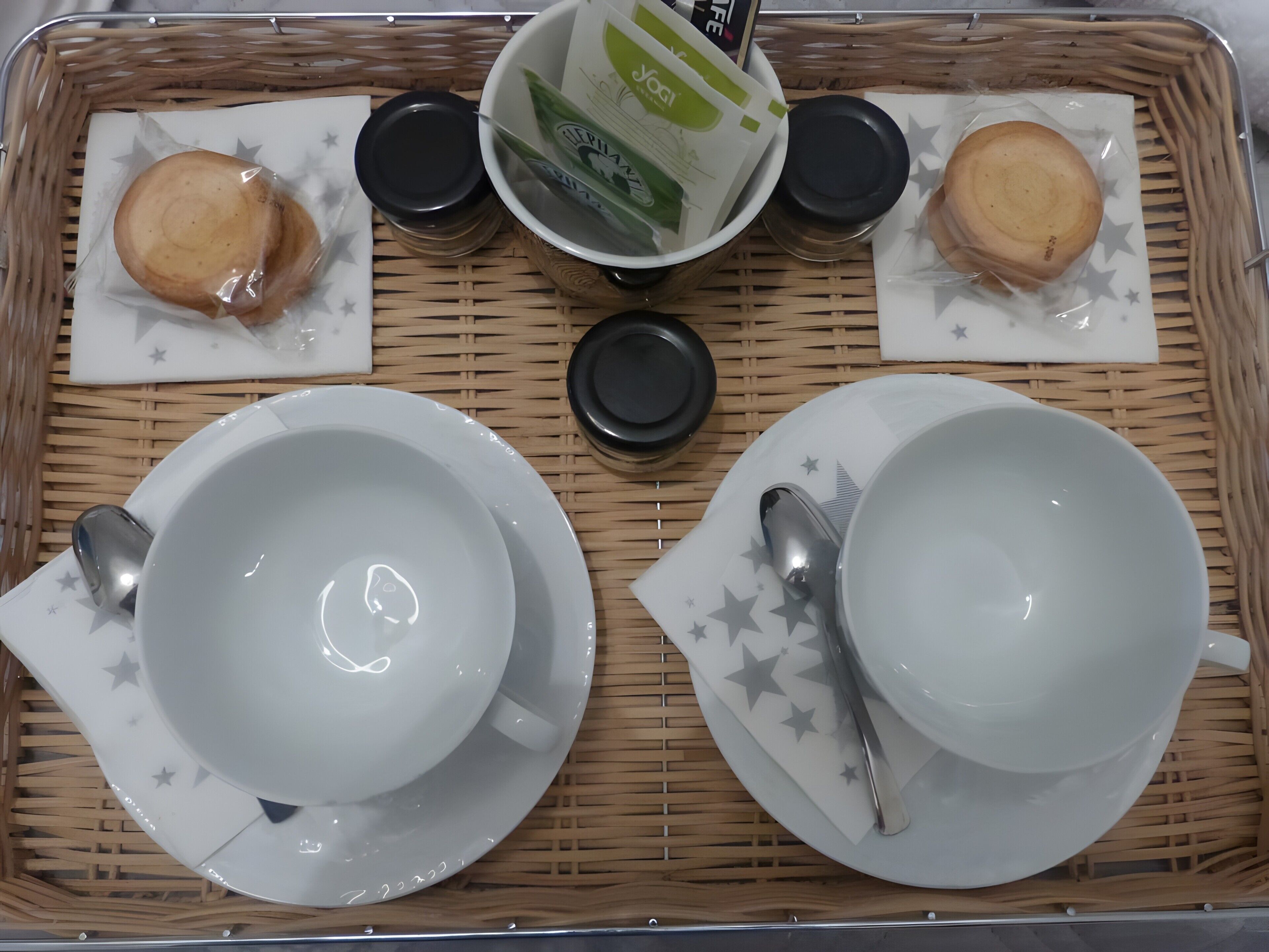Una bandeja con un juego de platos, tazones y tazas, junto con una cuchara y un recipiente pequeño, todo colocado sobre un tapete tejido.