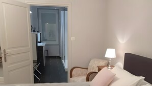 A hotel room with a bed, pillows, a bedside lamp, a chair, and a view of the hallway and bathroom.