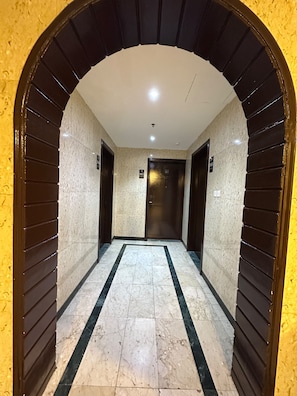 A hallway with a marble floor, dark wooden doors, and a yellow wall. - Durrat Al-Ijaba Hotel (Makkah)