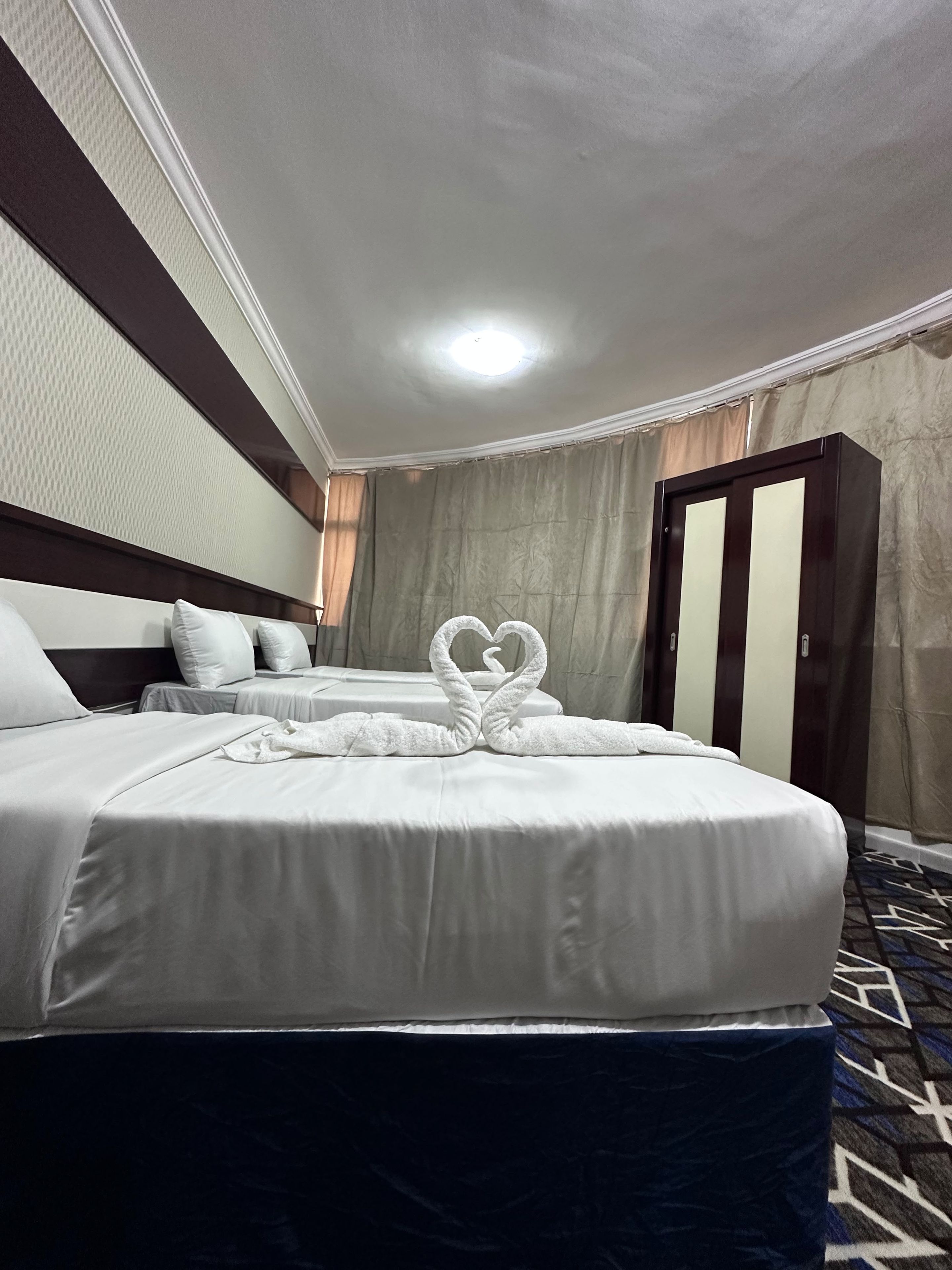 A hotel room with two beds, a headboard, a wardrobe, and a patterned carpet.