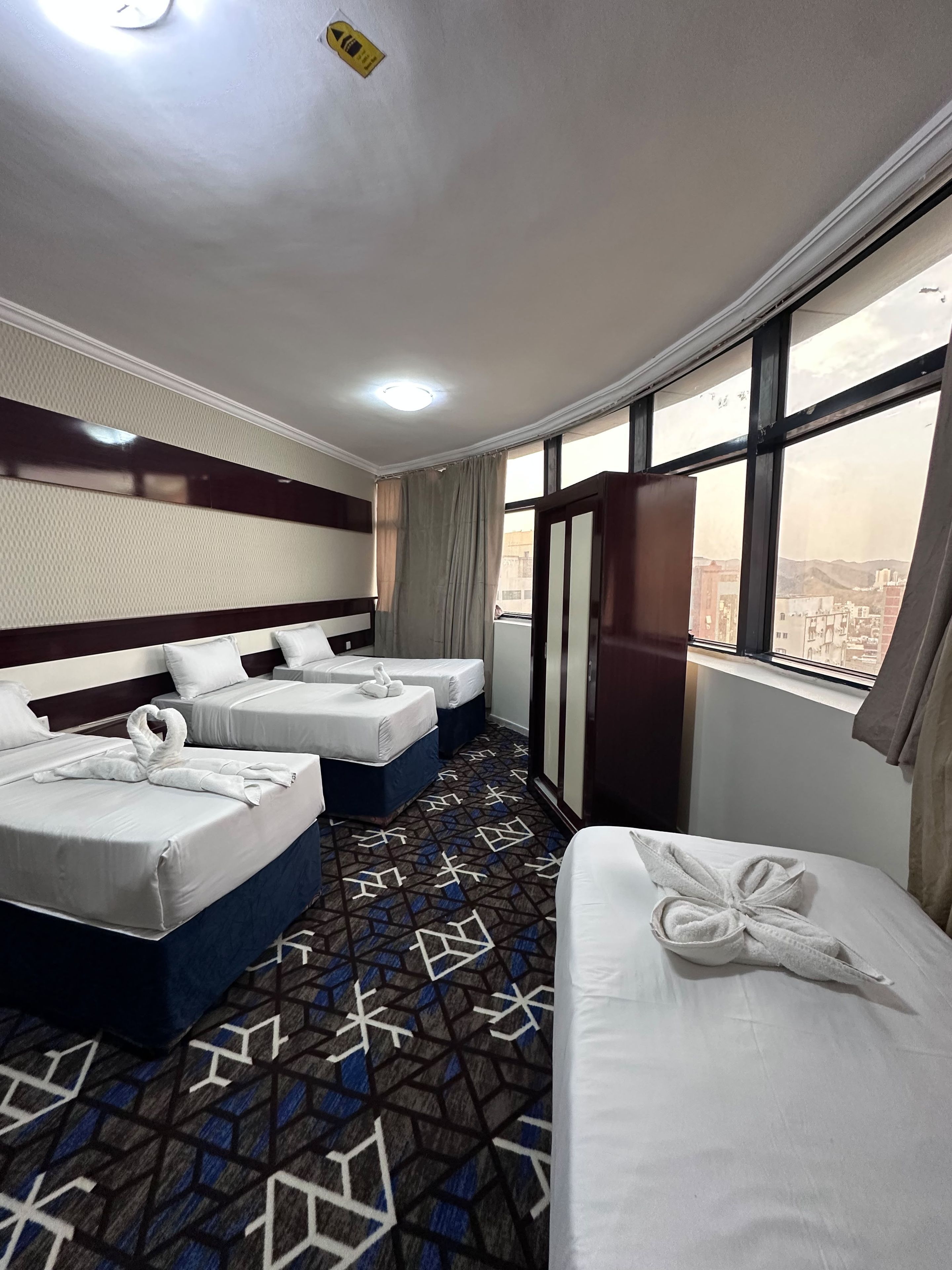 Habitación de hotel con dos camas, un ventanal grande y una alfombra estampada.