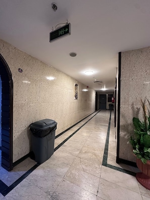 A corridor with a trash bin, directional sign, and a potted plant. - Durrat Al-Ijaba Hotel (Makkah)