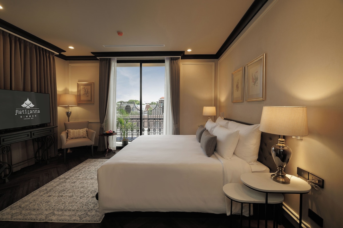 A hotel room with a large bed, a TV, a desk, and a view of the city.