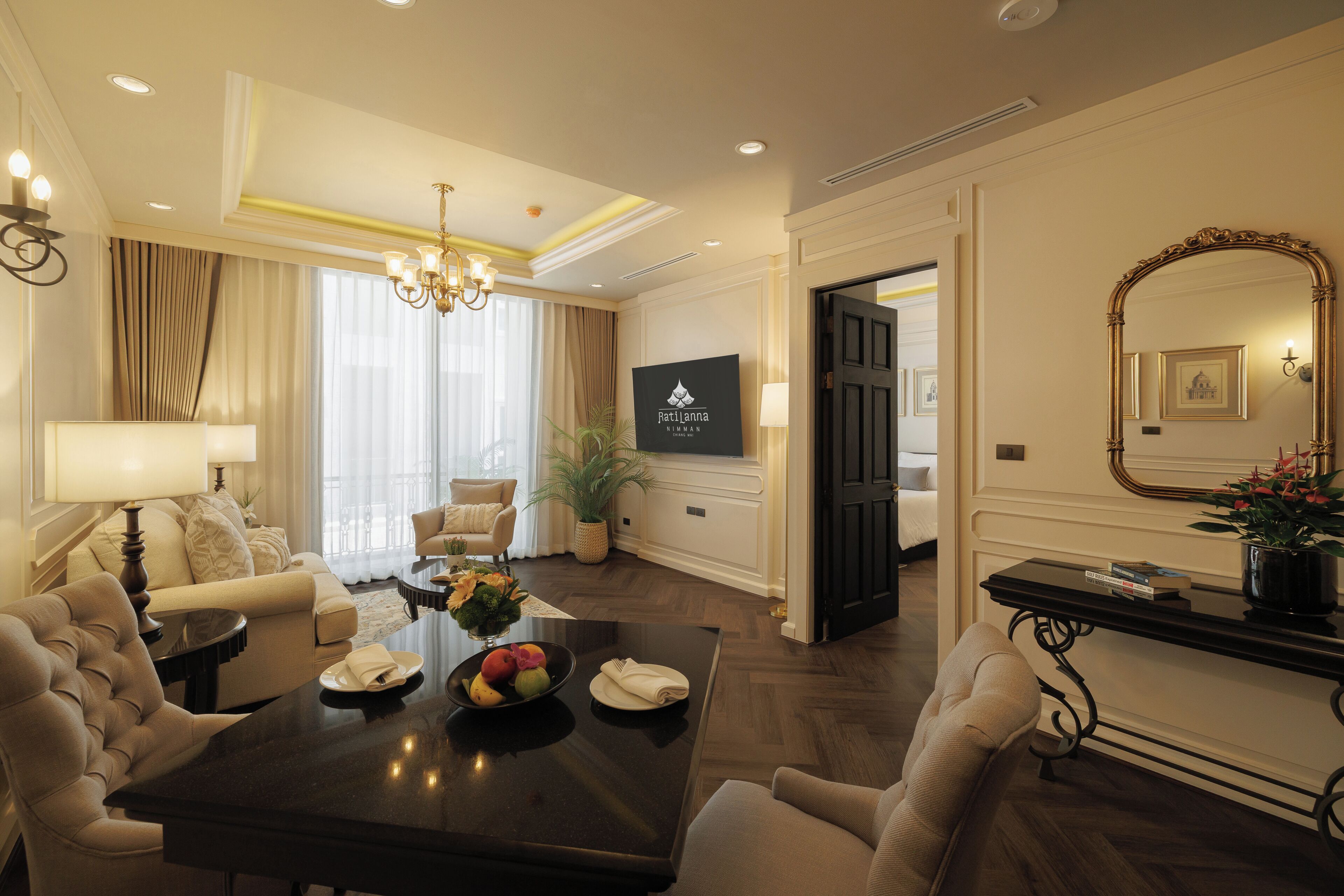 Habitación de hotel con comedor, sofá, candelabro y televisor en la pared.