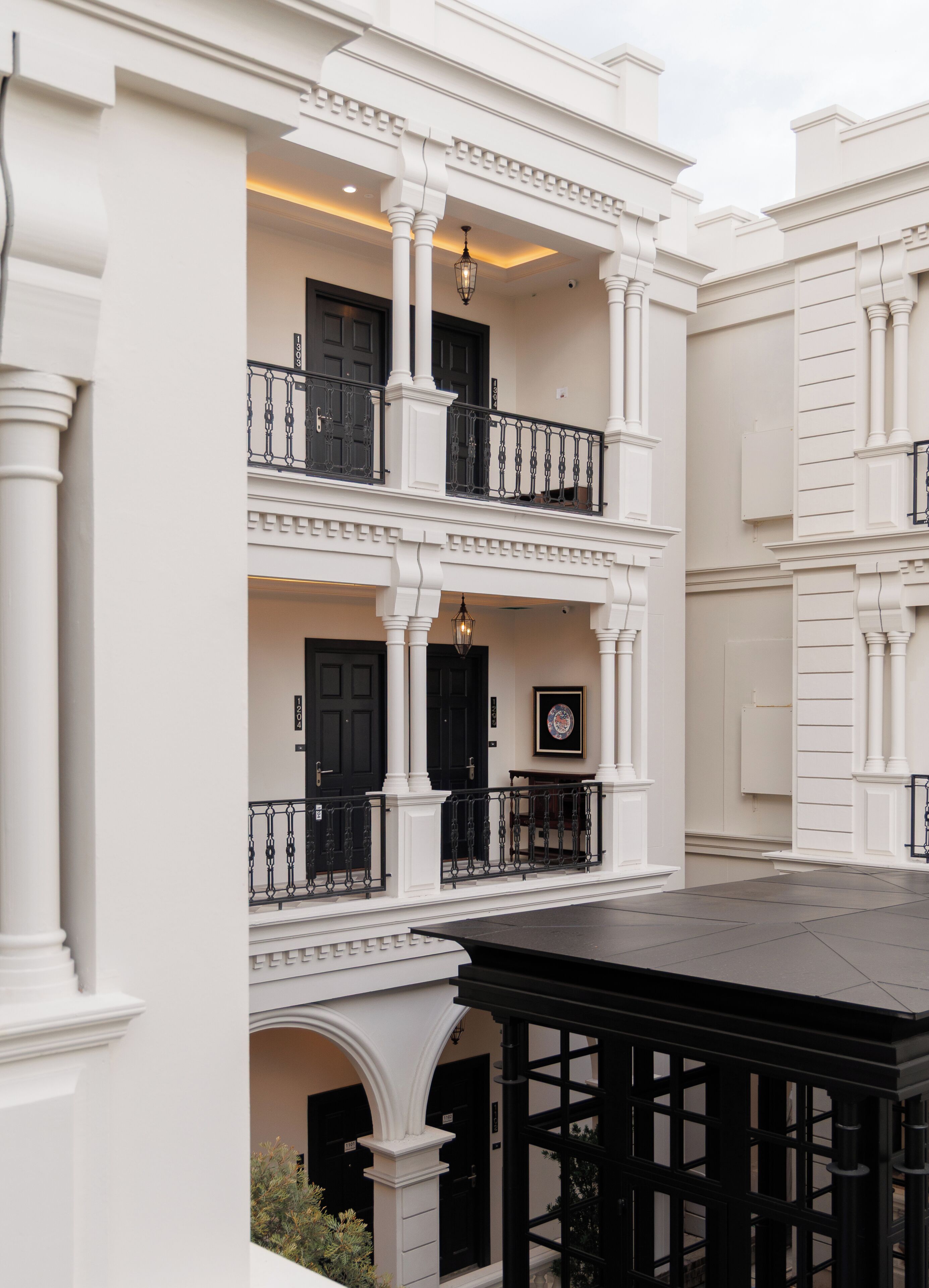 Un edificio de varios pisos con paredes exteriores blancas, ventanas de marco negro y un balcón con barandillas negras.