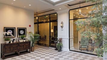 A lobby with a checkered floor, a wooden console table with decorative items, and a large window with a view of the interior.