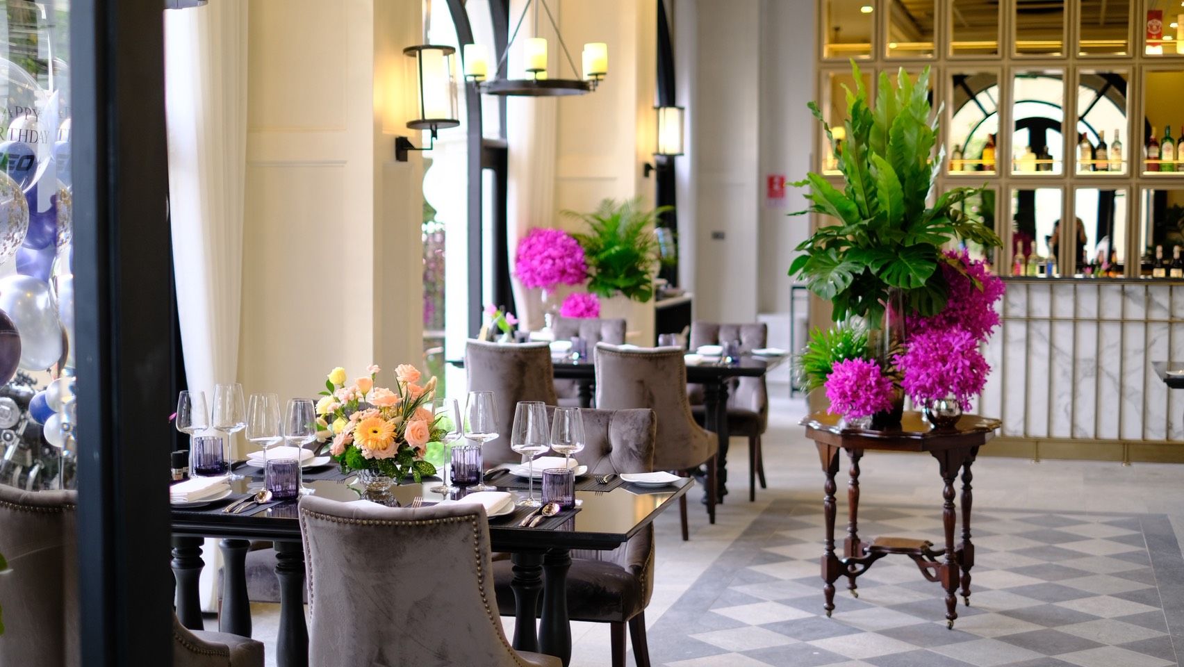 Un comedor con mesas dispuestas para el servicio, sillas y arreglos florales decorativos.