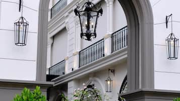 An arched entrance to a building with a balcony, outdoor seating area, and hanging lanterns.