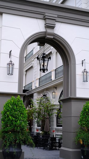 Una entrada arqueada a un edificio con balcón, zona de estar al aire libre y faroles colgantes.