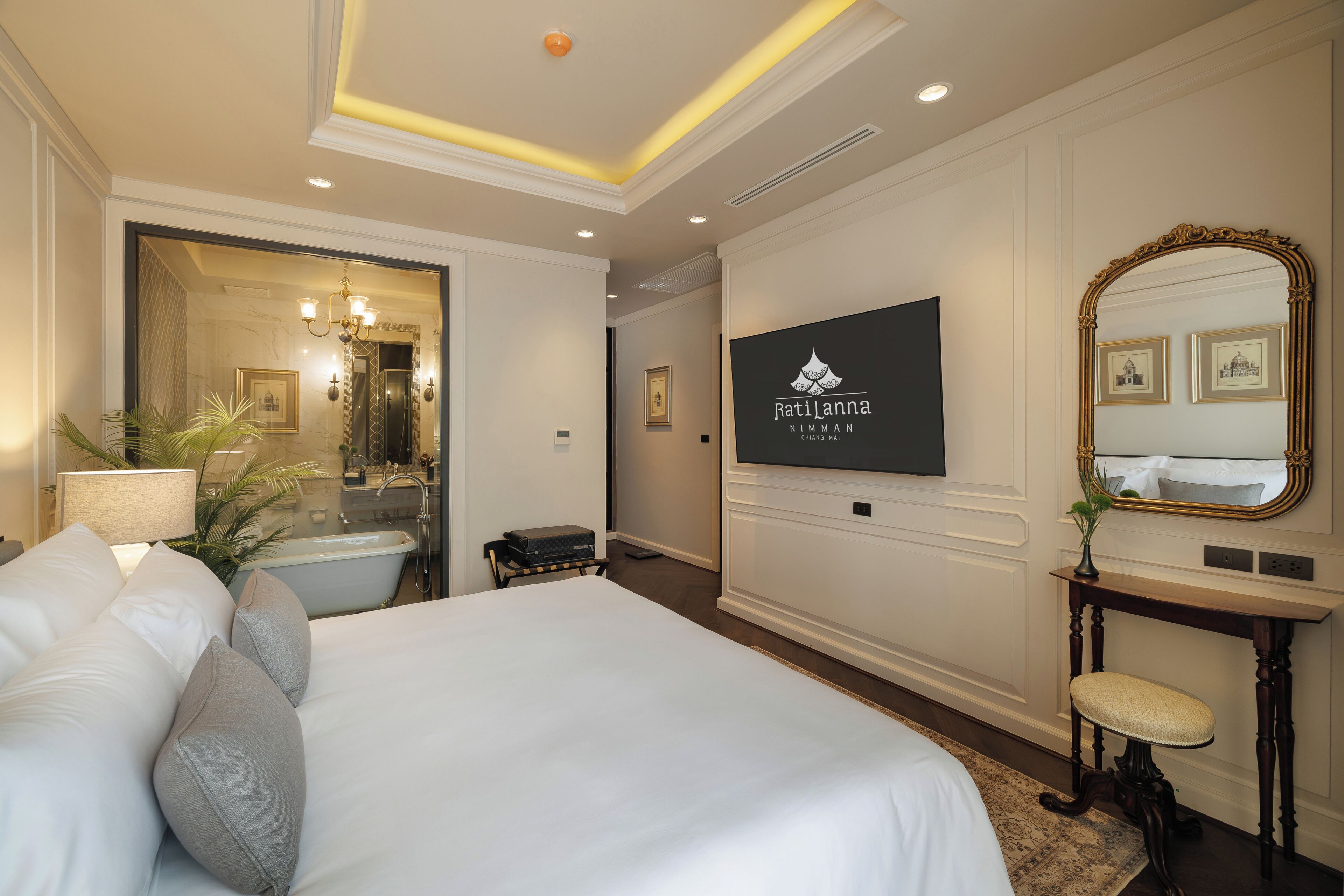 Habitación de hotel con una cama grande, televisión, espejo y baño con bañera.