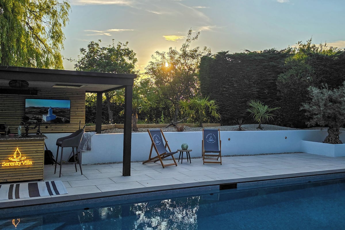 A pool area with a wooden bar, two lounge chairs, and a pergola.
