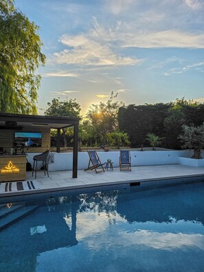 Un área de piscina con un bar de madera, dos sillones de descanso y una pérgola.