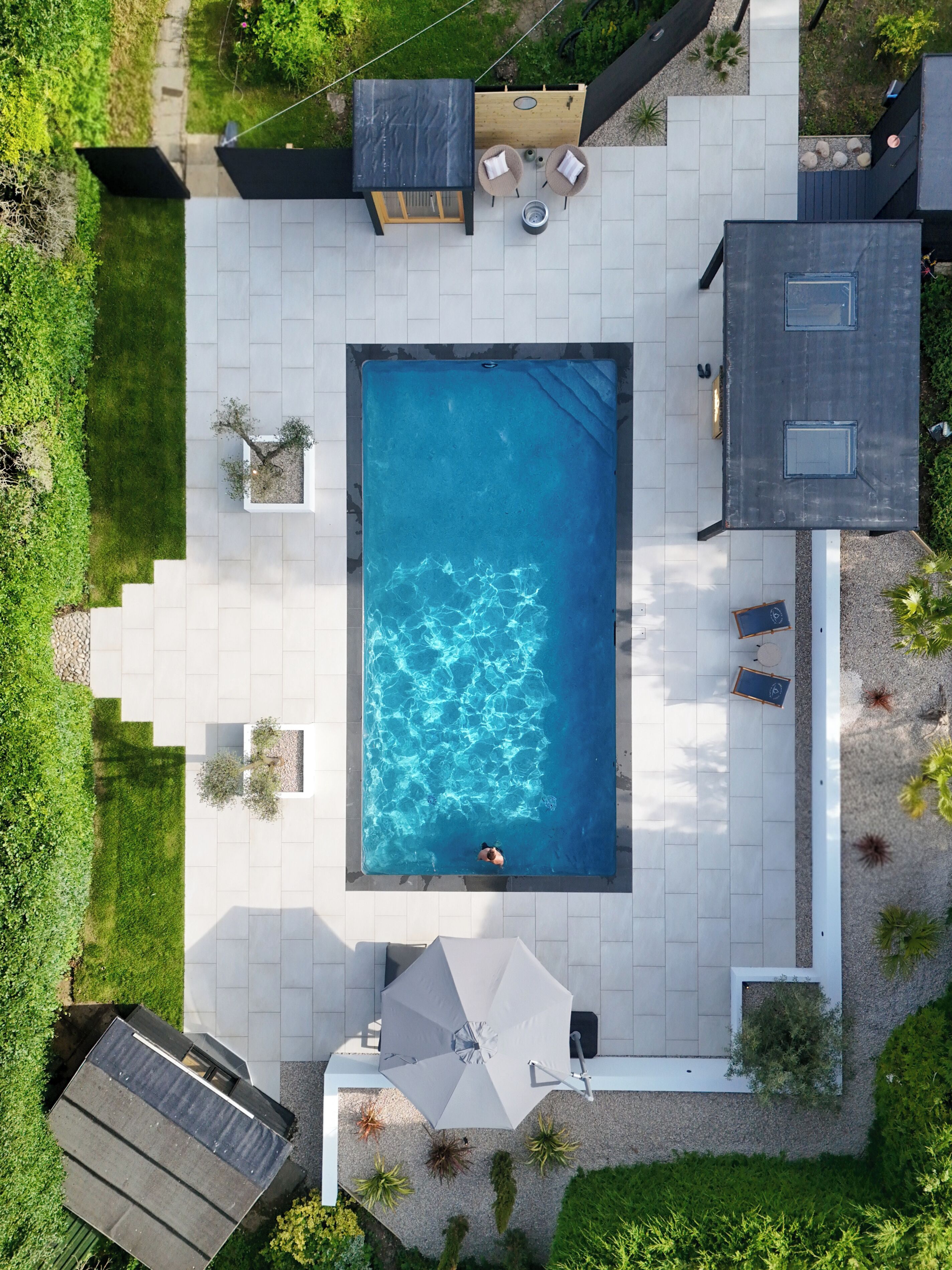A rooftop swimming pool with a person swimming, surrounded by a patio area with seating and a small garden.