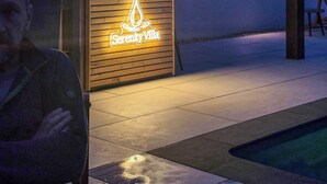 A modern outdoor area with a pool, a wooden structure with a neon sign, and a television screen displaying a beach scene. - Serenity Villa (Beccles)