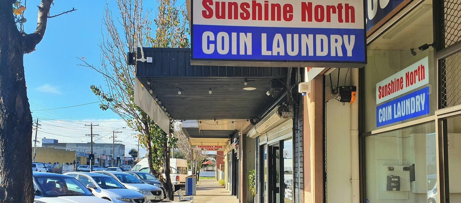 Una lavandería autoservicio llamada Sunshine North con un escaparate despejado y un corredor cubierto.