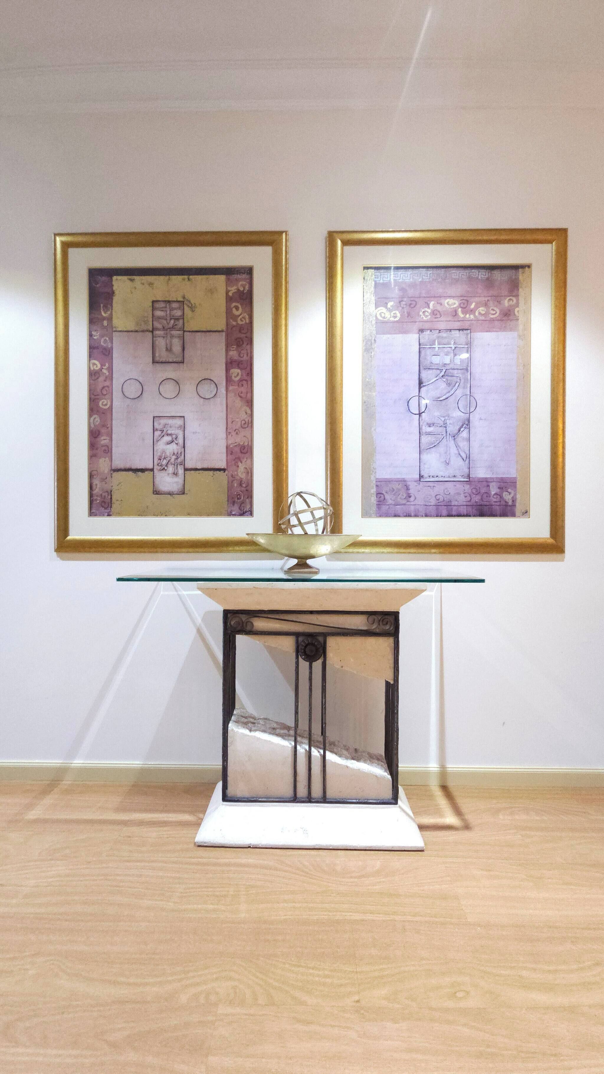 Una obra de arte en un marco colgada en una pared, una mesa de vidrio con base de metal y un suelo de madera.