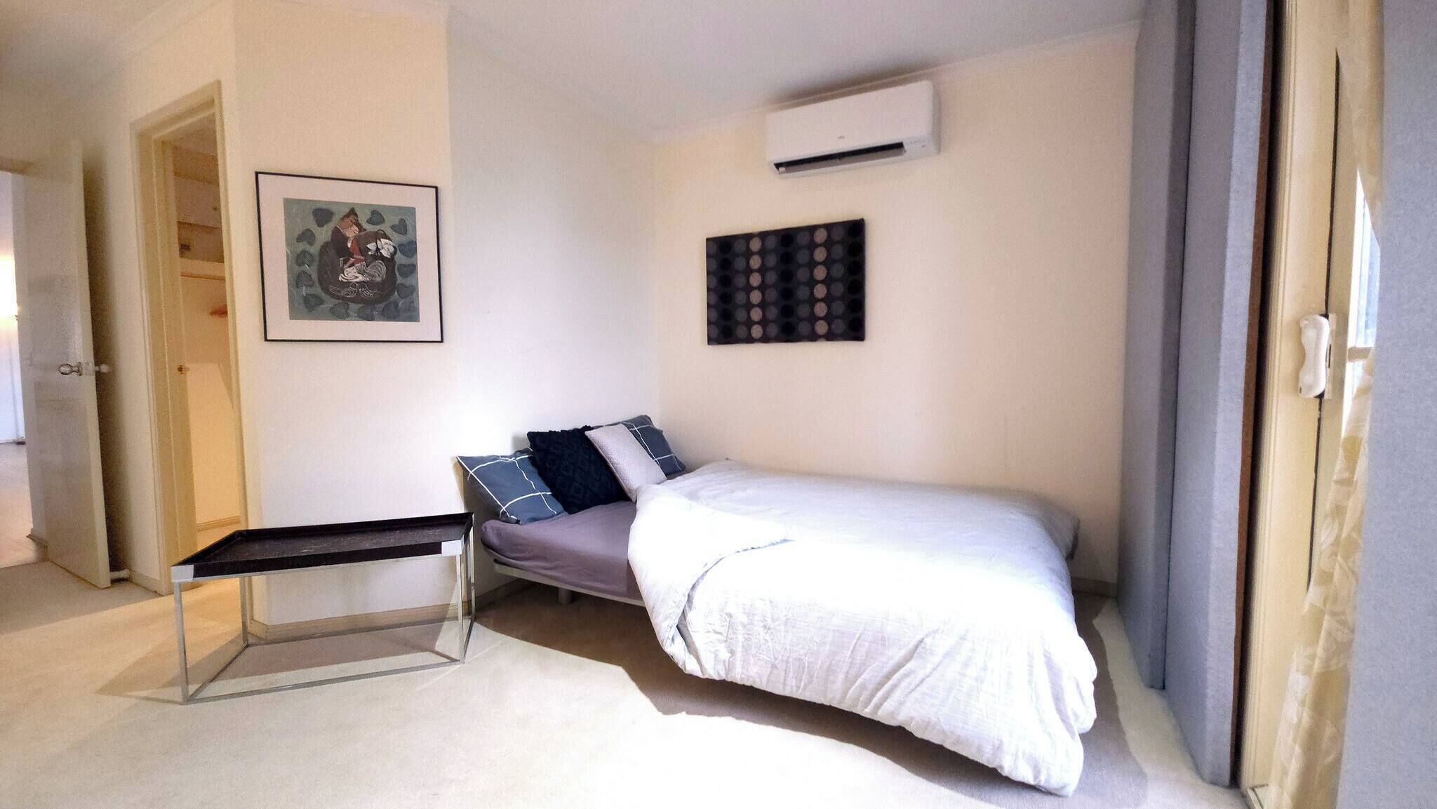 Een slaapkamer met een bed, een bureau, een stoel, een deur en een wandairconditioner.