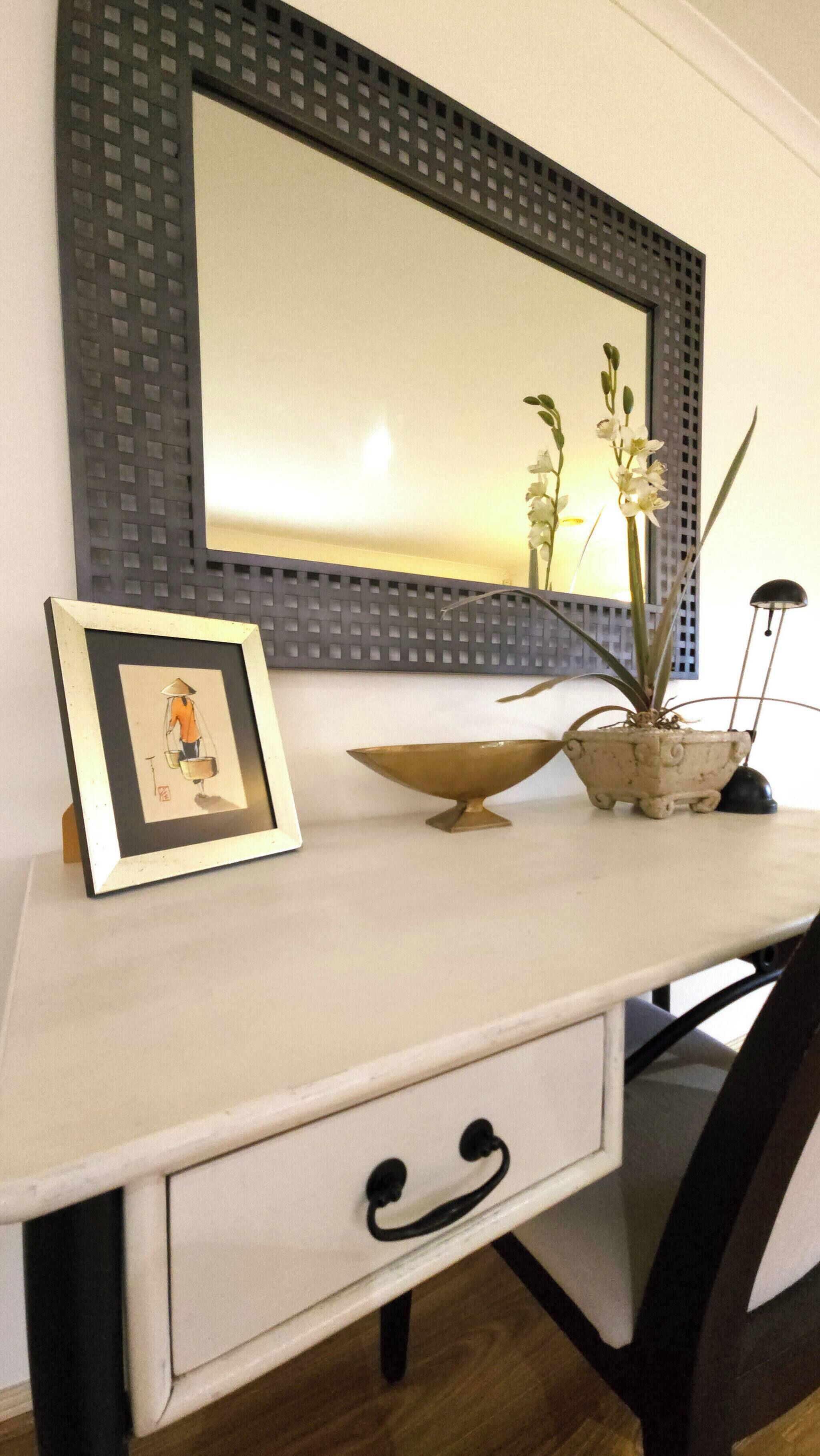 A desk with a framed picture, a potted plant, a bowl, and a lamp.