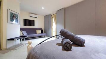 Un dormitorio con cama, sofá, un cuadro y un equipo de aire acondicionado.