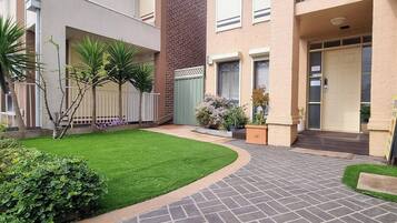 A courtyard with a well-maintained lawn, a brick pathway, and a building with a green gate and a door.