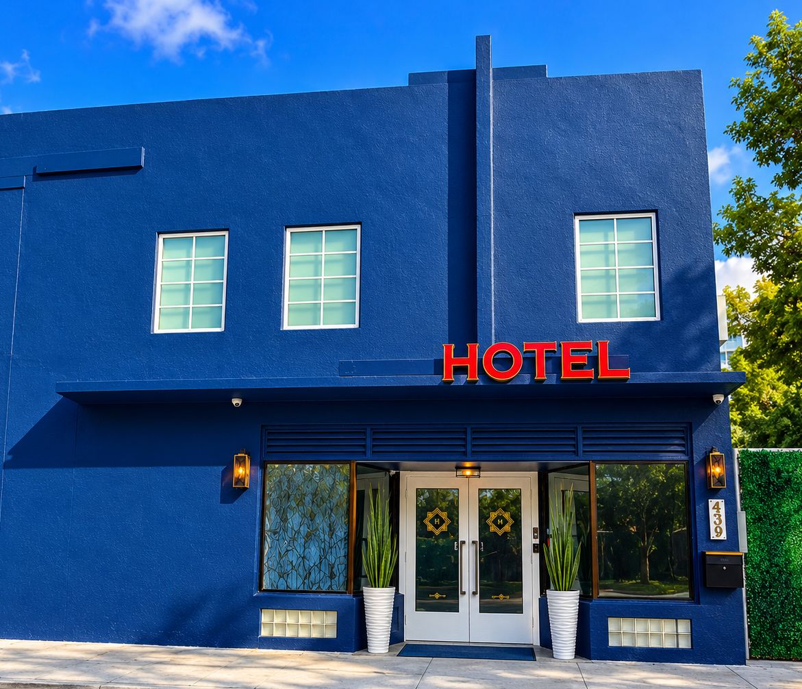 Un bâtiment bleu avec une enseigne indiquant « HÔTEL », de grandes fenêtres et une entrée fermée par un portail.