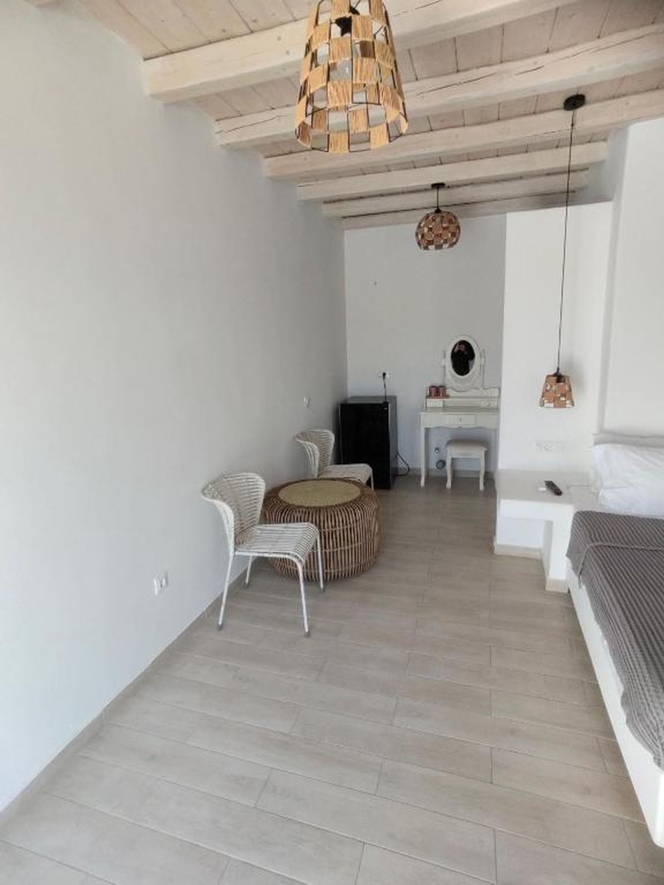 Ein Zimmer mit einem Bett, einem runden Korbstuhl, einem kleinen weißen Tisch und einer Pendelleuchte.
