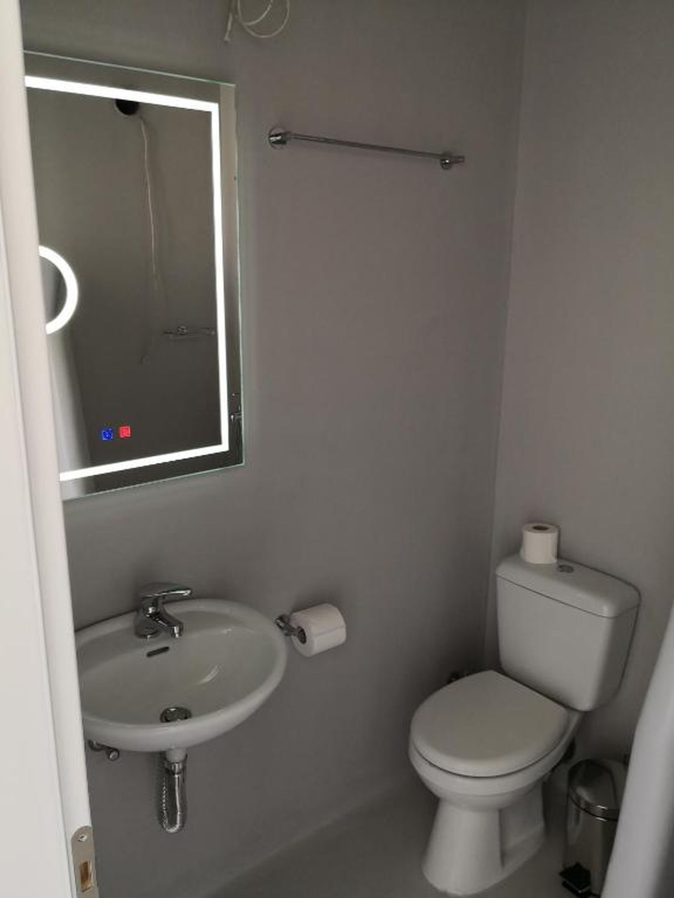 A bathroom with a white sink, a toilet, a mirror with a light, and a towel rack.