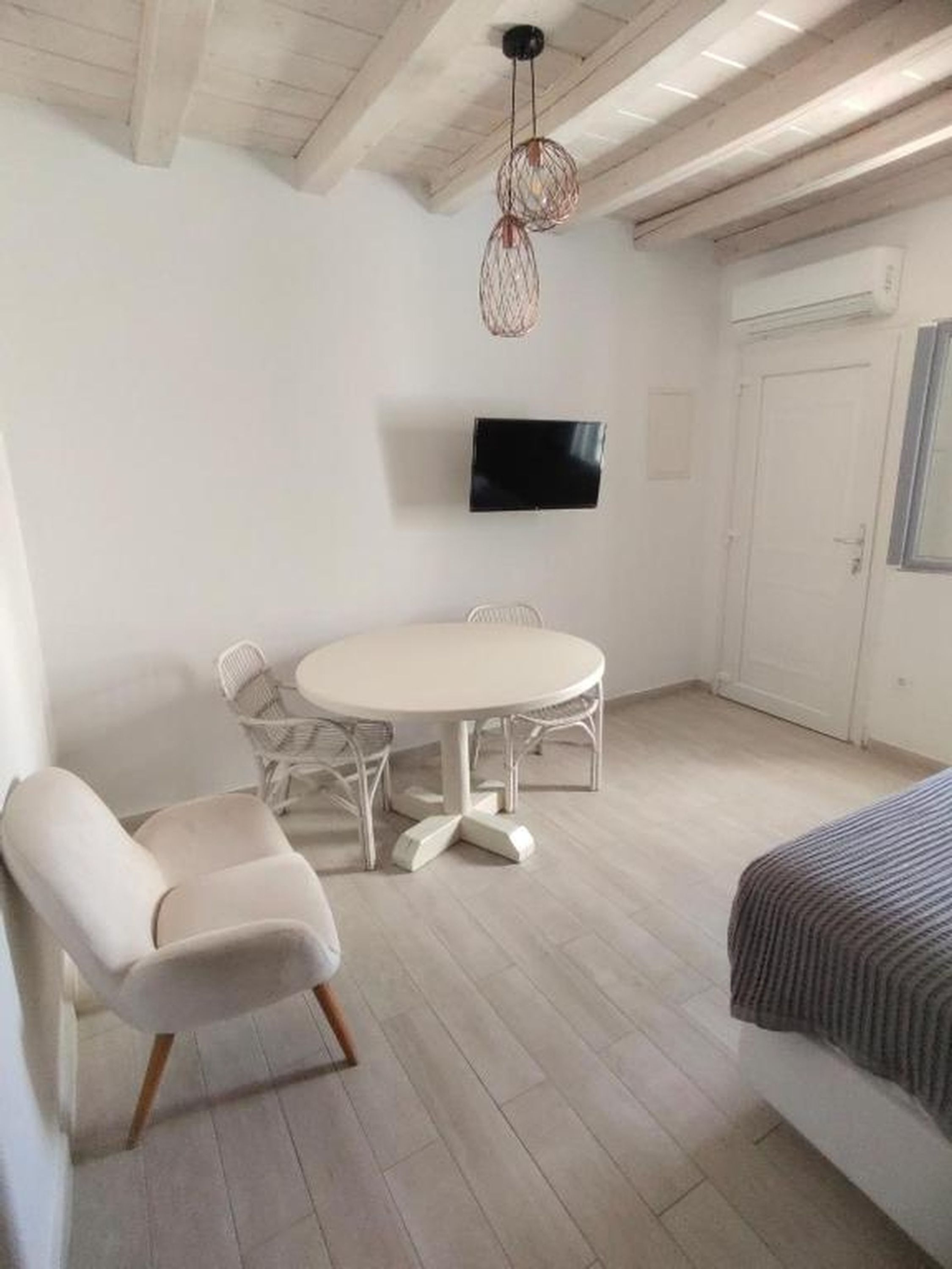A room with a round table, two chairs, a sofa, a television, and a door.