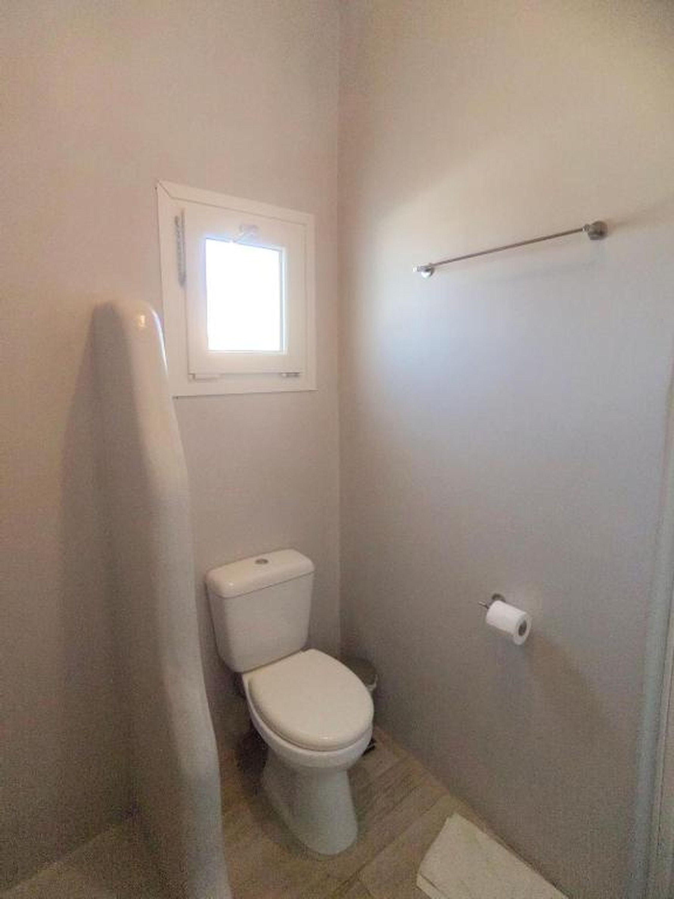 A small, white bathroom with a toilet, a window, and a towel rack.