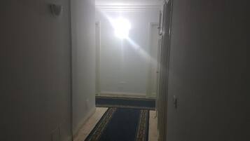 Un pasillo estrecho con alfombra estampada, paredes blancas y una puerta al final.