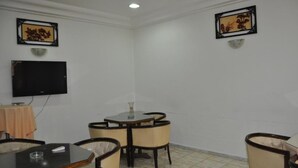 Una habitación con una televisión de pantalla plana montada en la pared, una mesa redonda con sillas, y dos cuadros en las paredes.