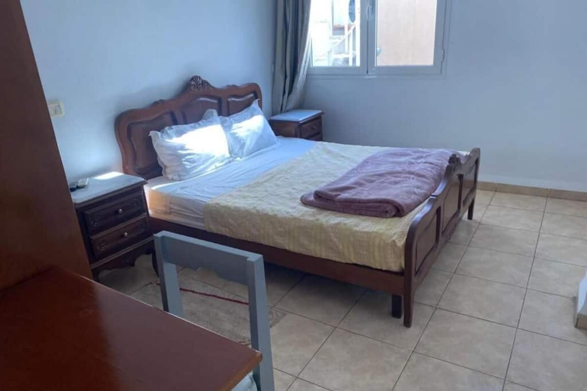 Un dormitorio con cama, mesitas de noche, una silla y una ventana.