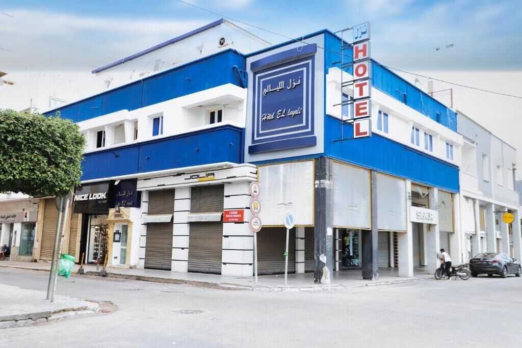 Un hotel con fachada azul y blanca, un letrero con texto en árabe y un escaparate con un anuncio que dice 'Nice Look'.