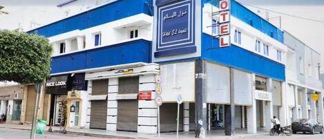 Un hotel con fachada azul y blanca, un letrero con texto en árabe y un escaparate con un anuncio que dice 'Nice Look'.