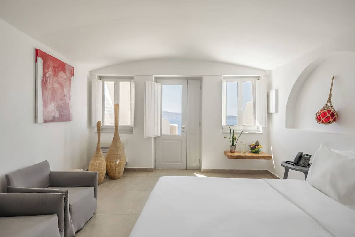 Ein Schlafzimmer mit einem Bett, einer Couch, einer großen Vase, einer Tür und Blick ins Freie.