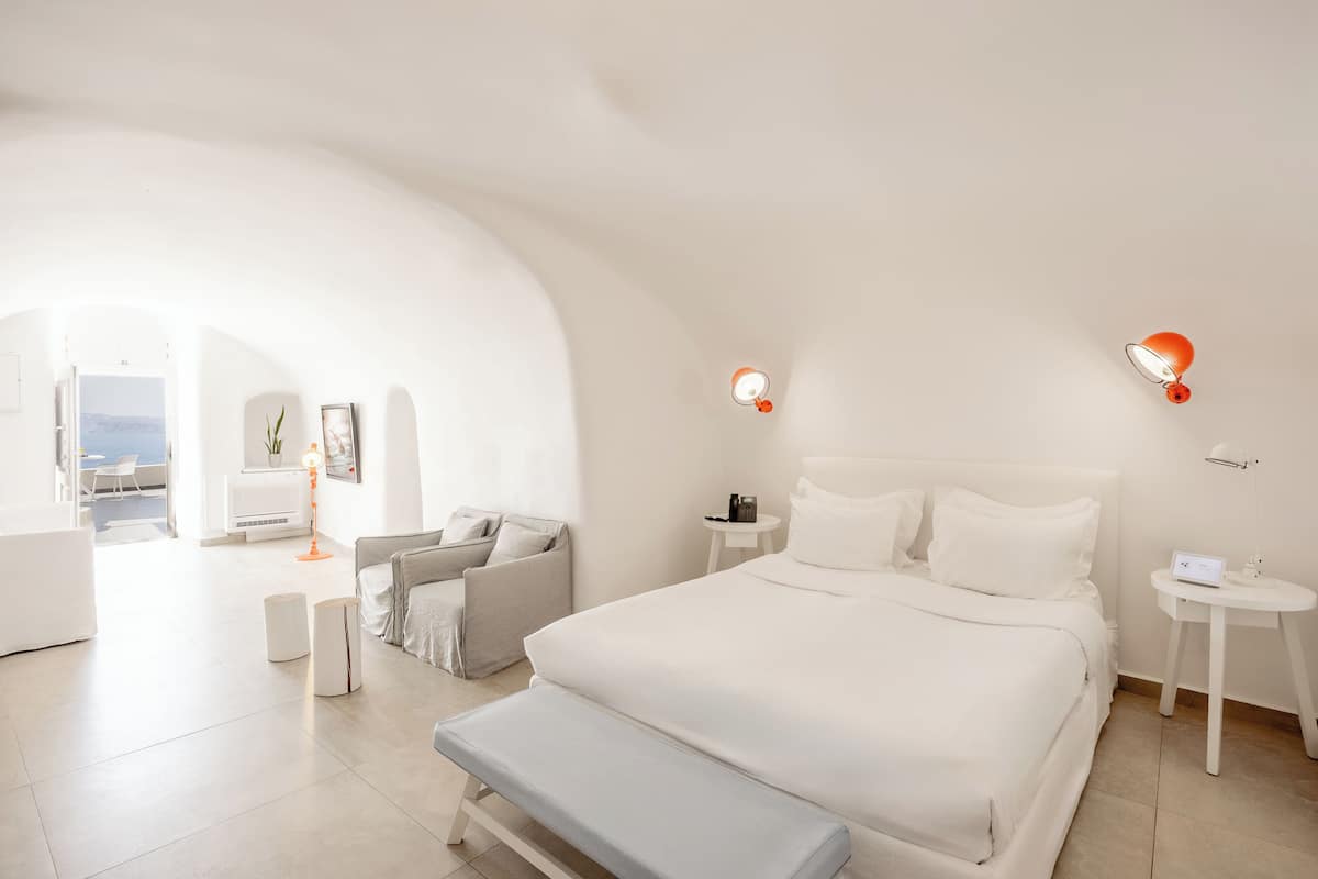 Ein modernes Hotelzimmer mit einem großen Bett, einer Bank, einem kleinen Tisch und Meerblick.