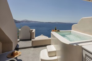 Un balcón con vista al mar, un jacuzzi y un sombrero sobre una mesa.